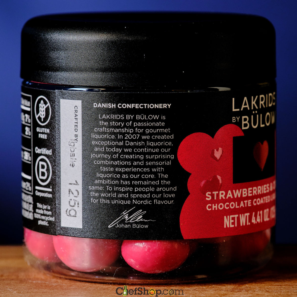 Jar of Lakrids by Bülow strawberry and chocolate coated liquorice on a wooden surface with a blue background