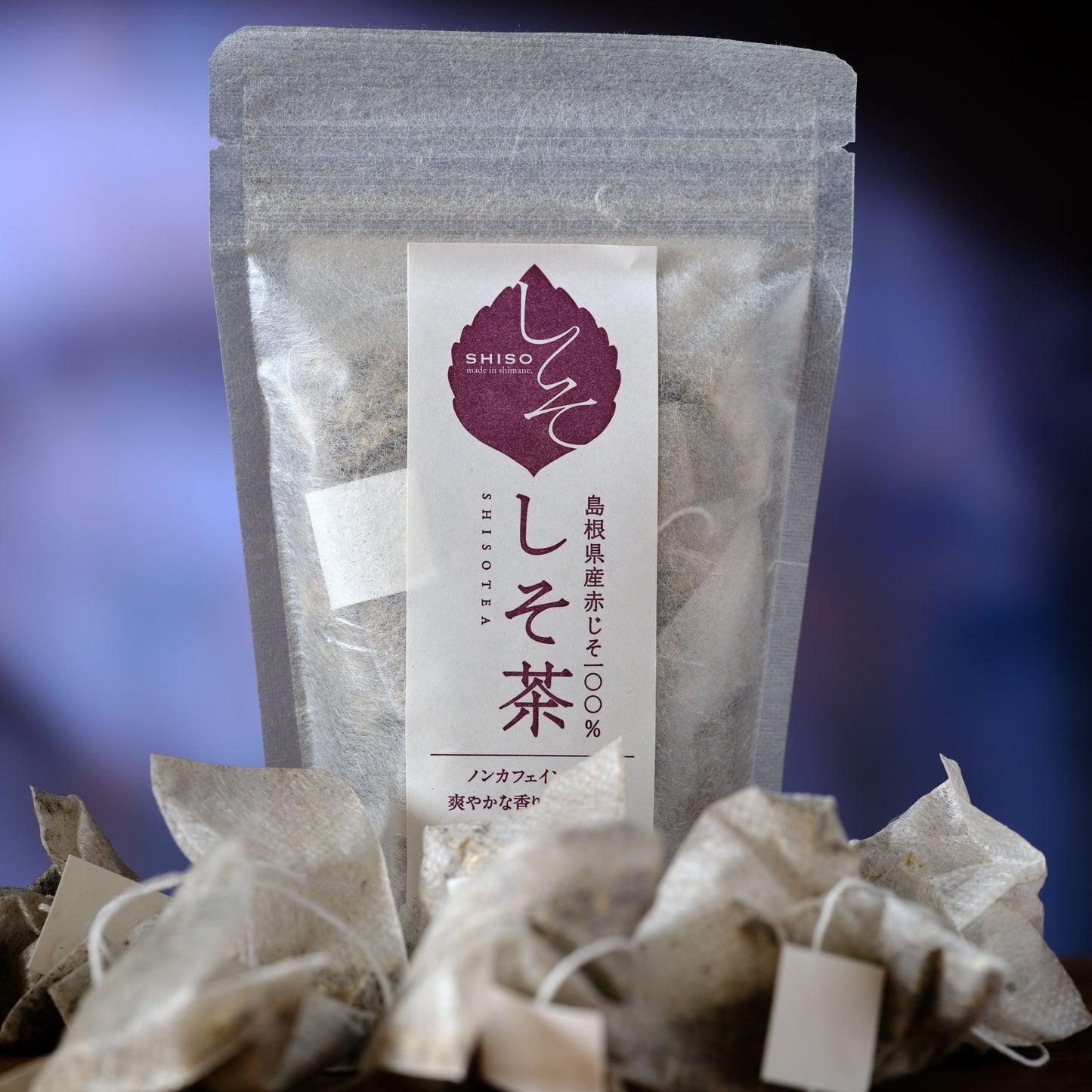 Shiso Tea - Japanese Perilla - Tea package with a label featuring Japanese text and a purple leaf symbol on a blurred blue background.