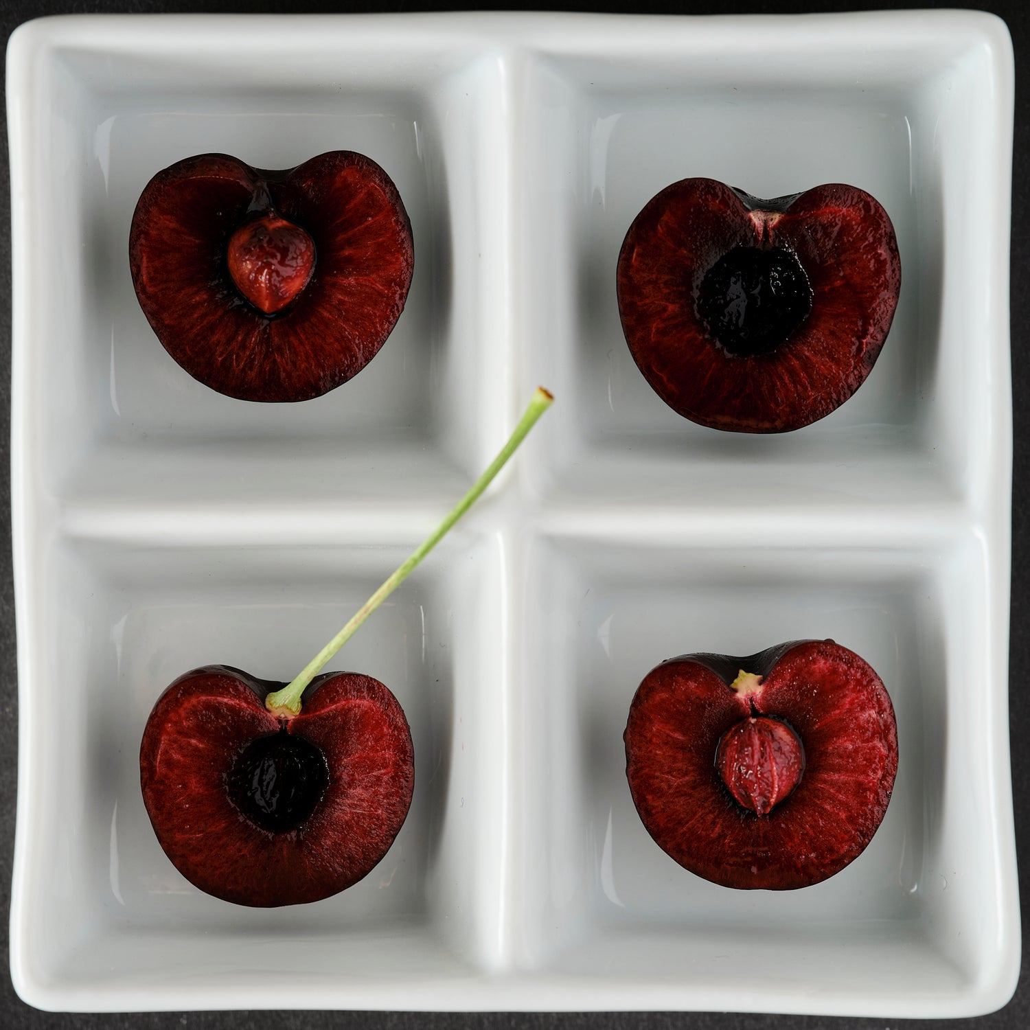 Black Pearl Cherry Four halves of a cherry on a white divided plate. ChefShop