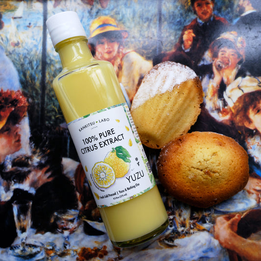 Kankitsu Labo Citrus Extract Bottle of 100% Pure Citrus Extract Yuzu with Madeleines on a tablecloth with people in the background