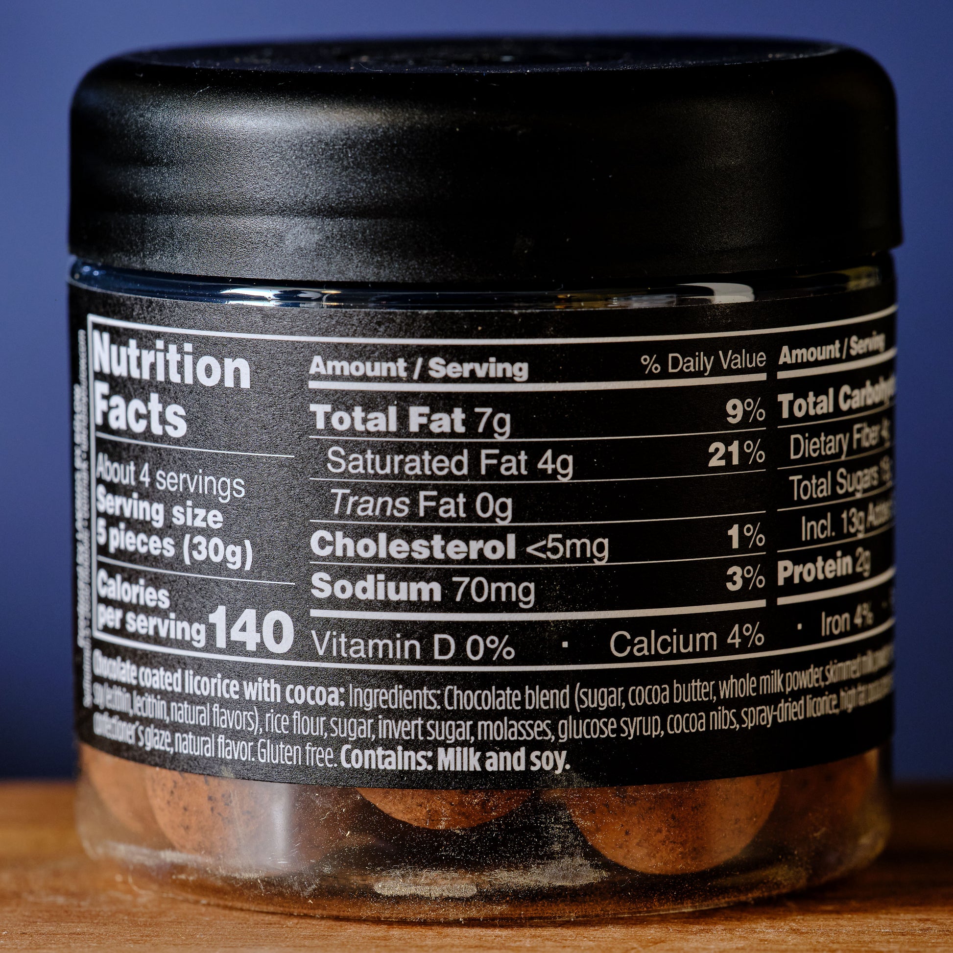 Jar of chocolate-coated licorice with nutrition label on a wooden surface