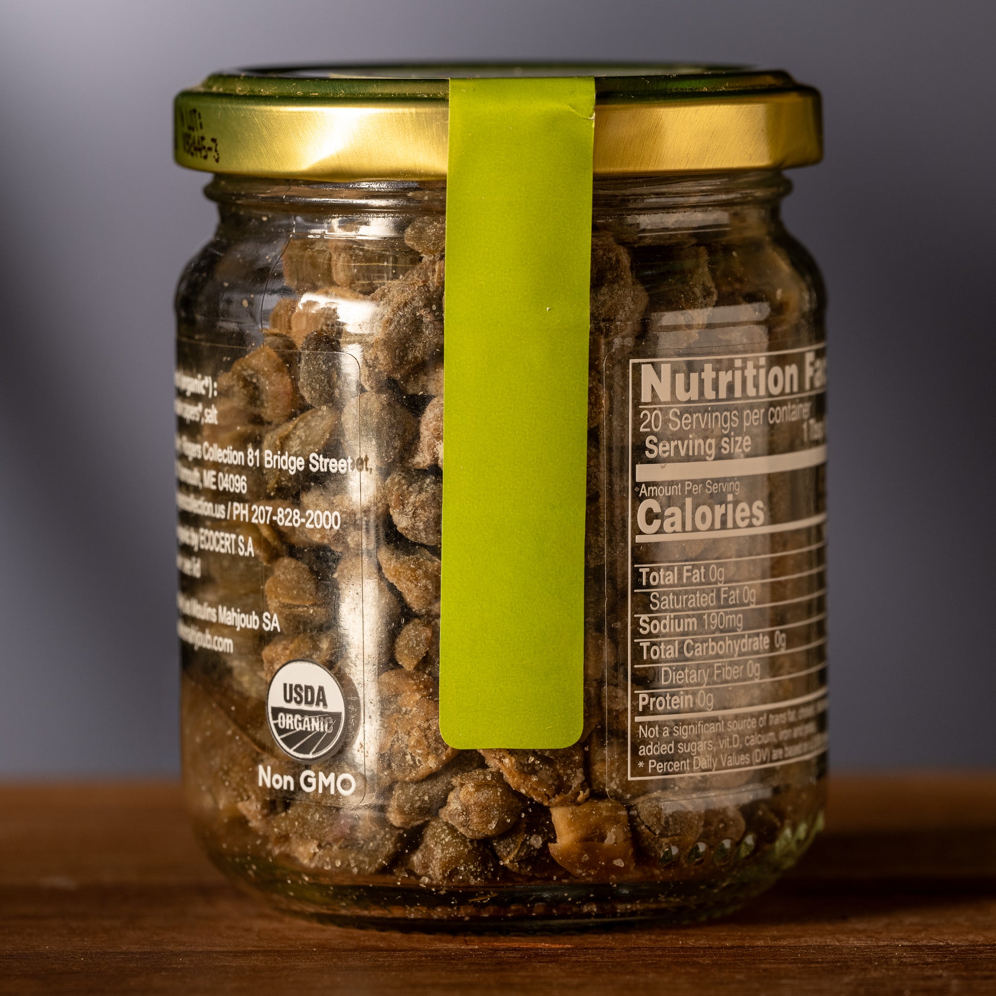 Glass jar with a green lid containing capers, showing nutrition facts label.
