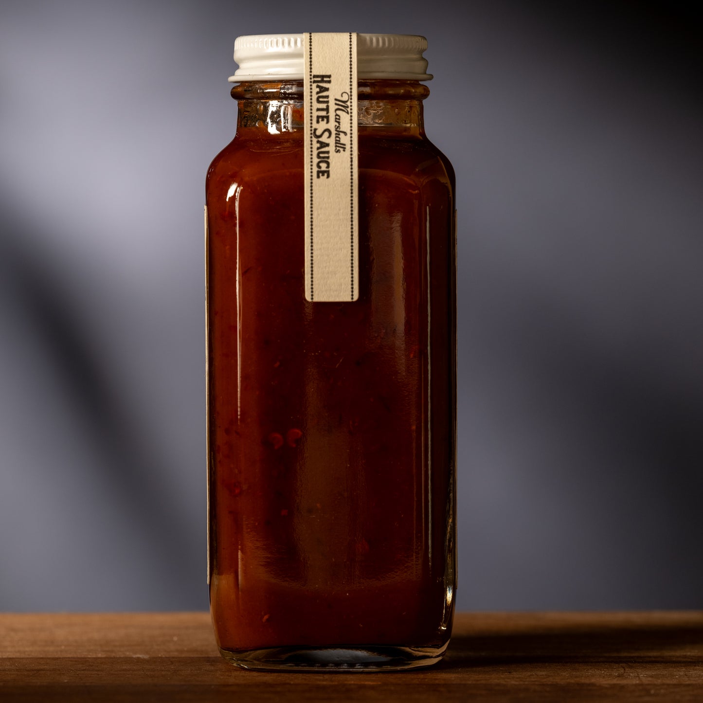 Jar of sauce with a label on a wooden surface and gray background