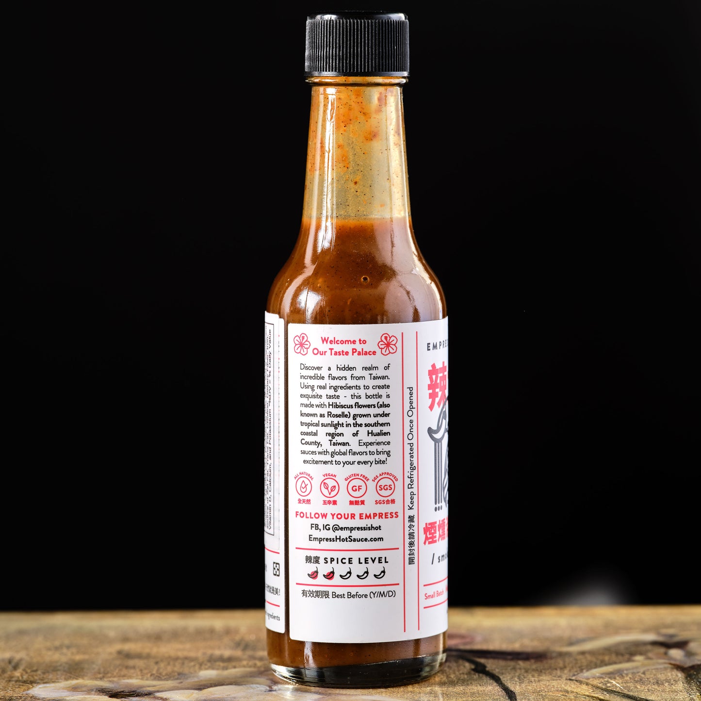 Empress Smoky Hibiscus Hot Sauce Hot sauce bottle with a label on a wooden surface and black background