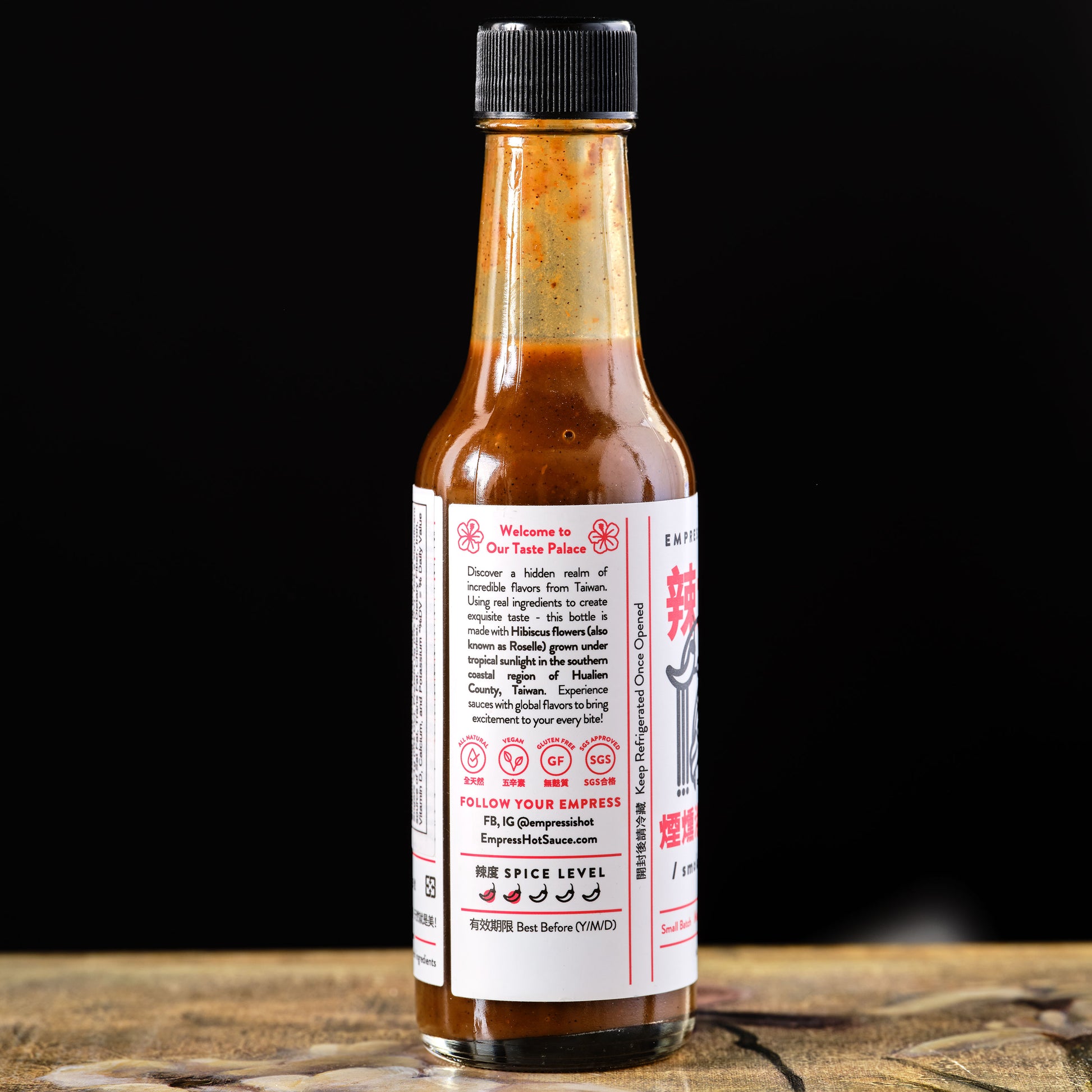 Empress Smoky Hibiscus Hot Sauce Hot sauce bottle with a label on a wooden surface and black background