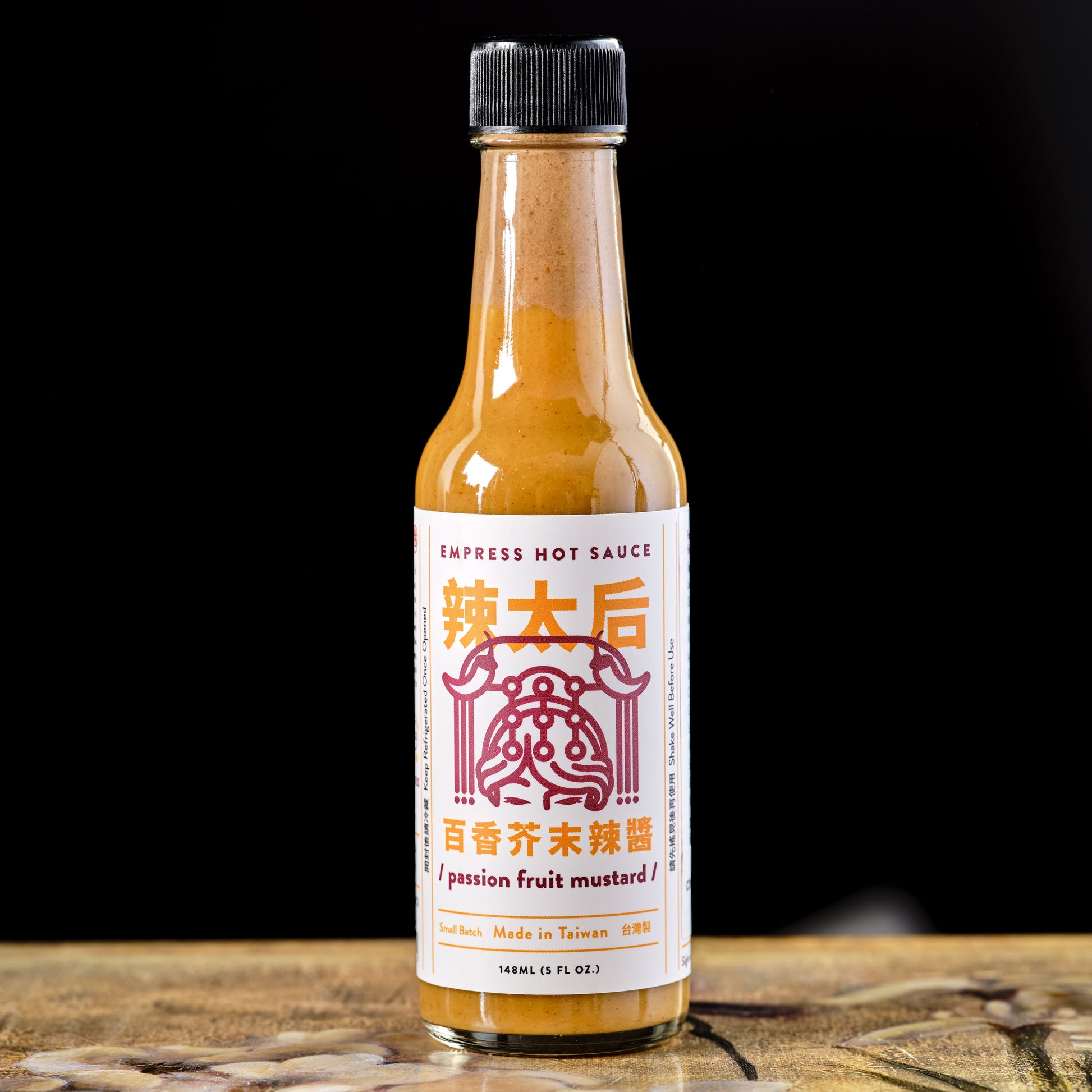 Bottle of Empress Hot Sauce on a wooden surface with a black background