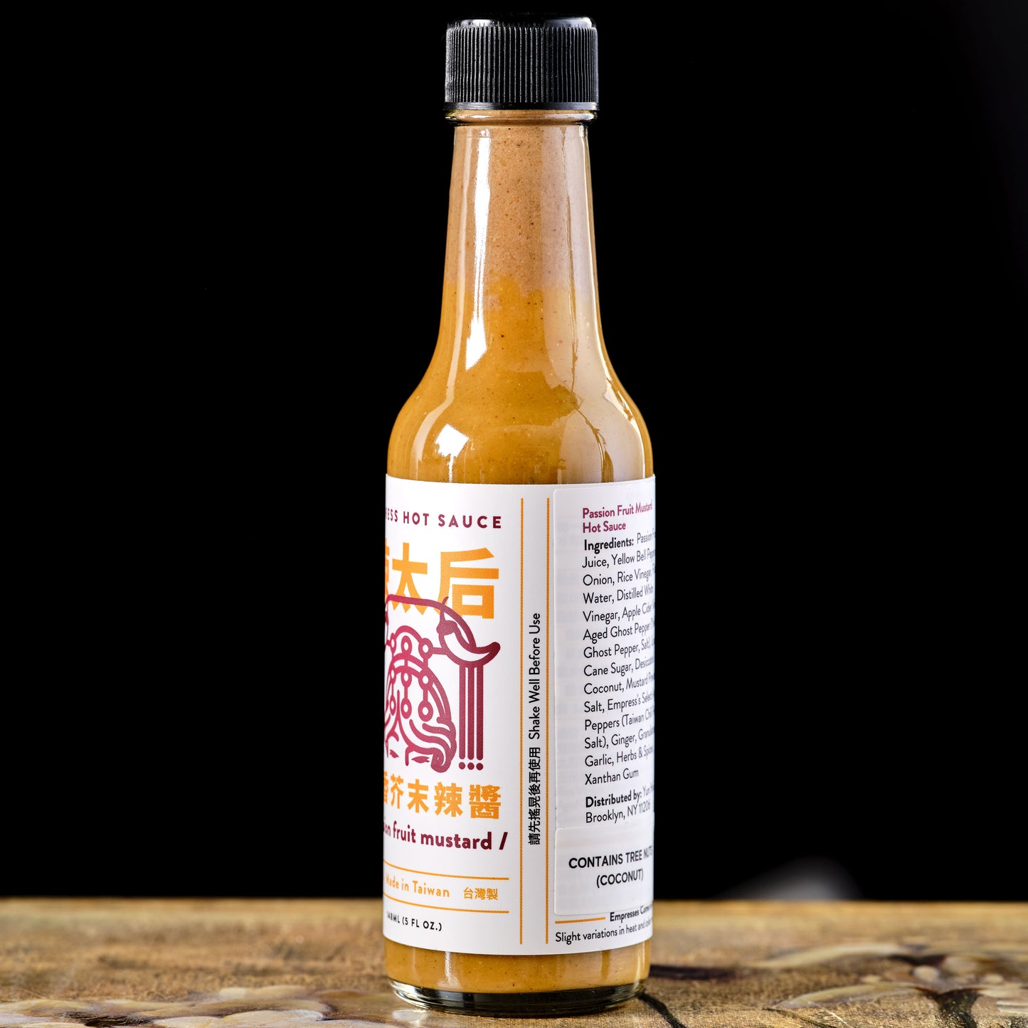 Hot sauce bottle with a label on a wooden surface and black background Empress Passion Fruit Mustard Hot Sauce