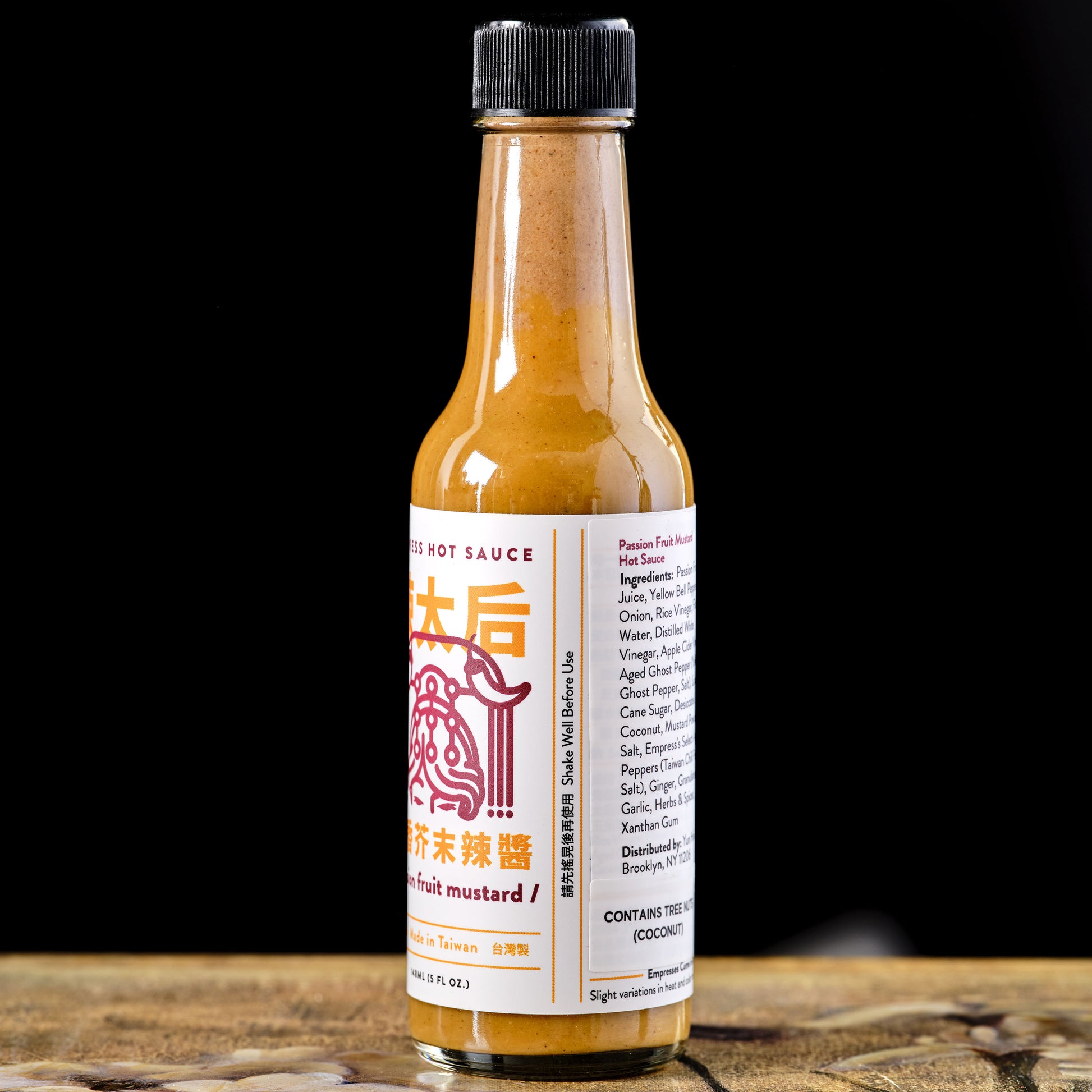 Hot sauce bottle with a label on a wooden surface and black background Empress Passion Fruit Mustard Hot Sauce