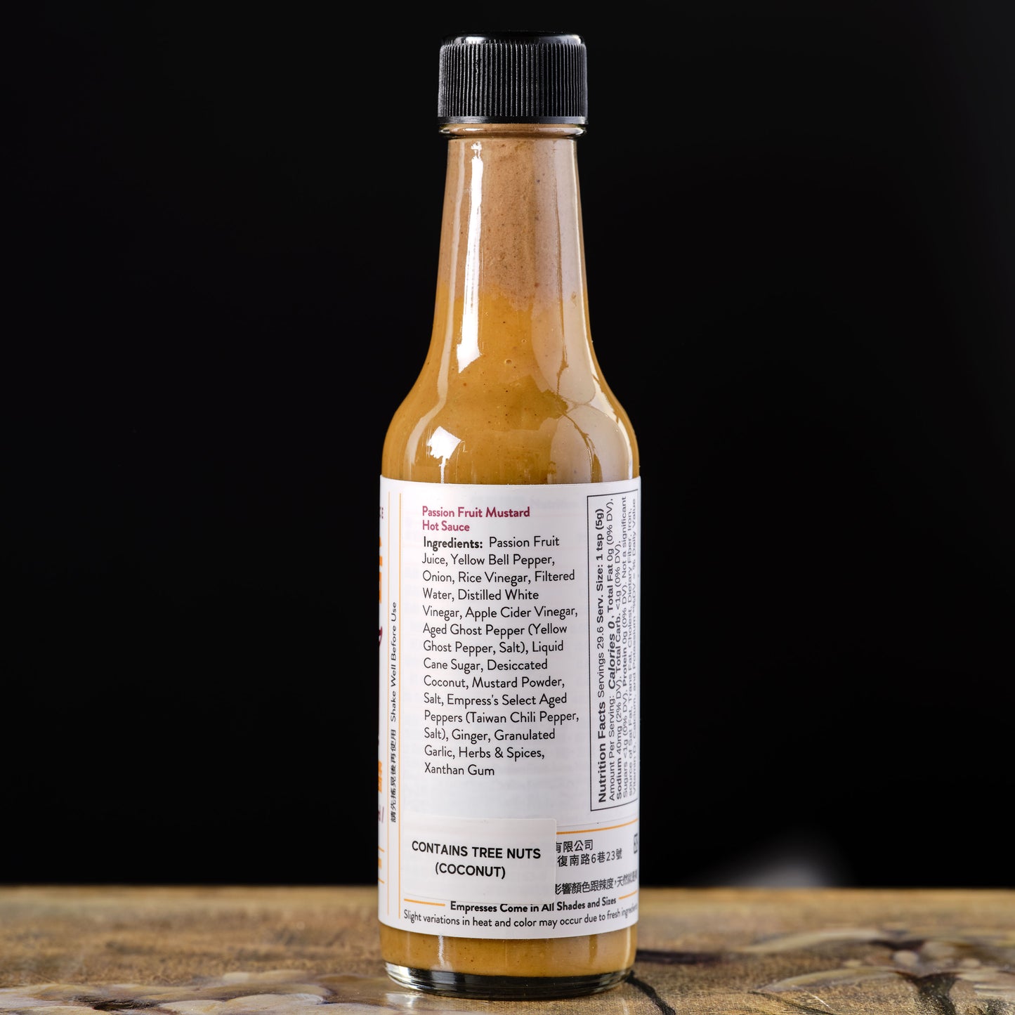 Bottle of hot sauce with a black cap on a wooden surface against a dark background Empress Passion Fruit Mustard Hot Sauce