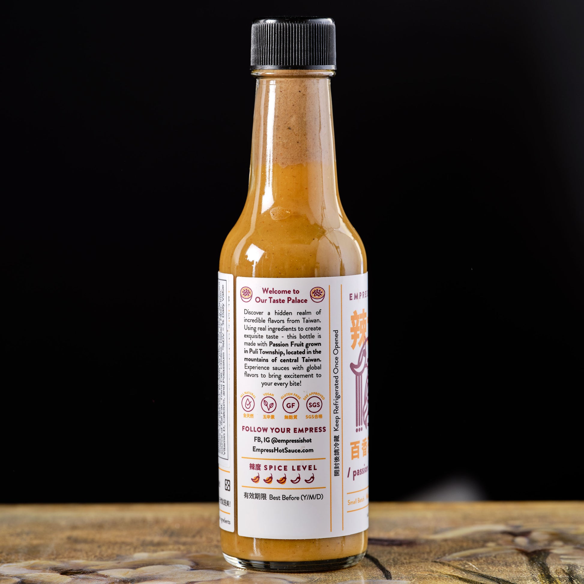 Hot sauce bottle with label on a wooden surface and black background Empress Passion Fruit Mustard Hot Sauce