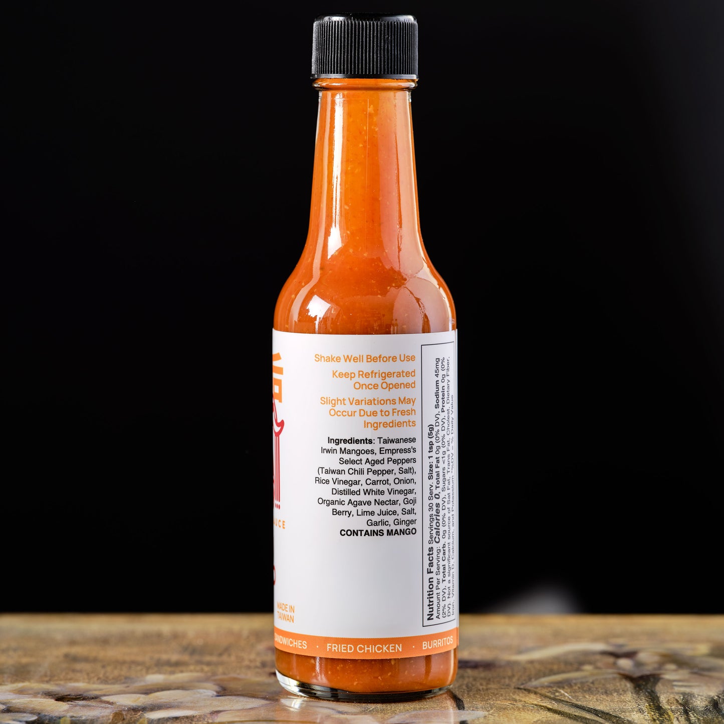 Empress Irwin Mango Hot Sauce Hot  Ingredients sauce bottle with label on a wooden surface and black background