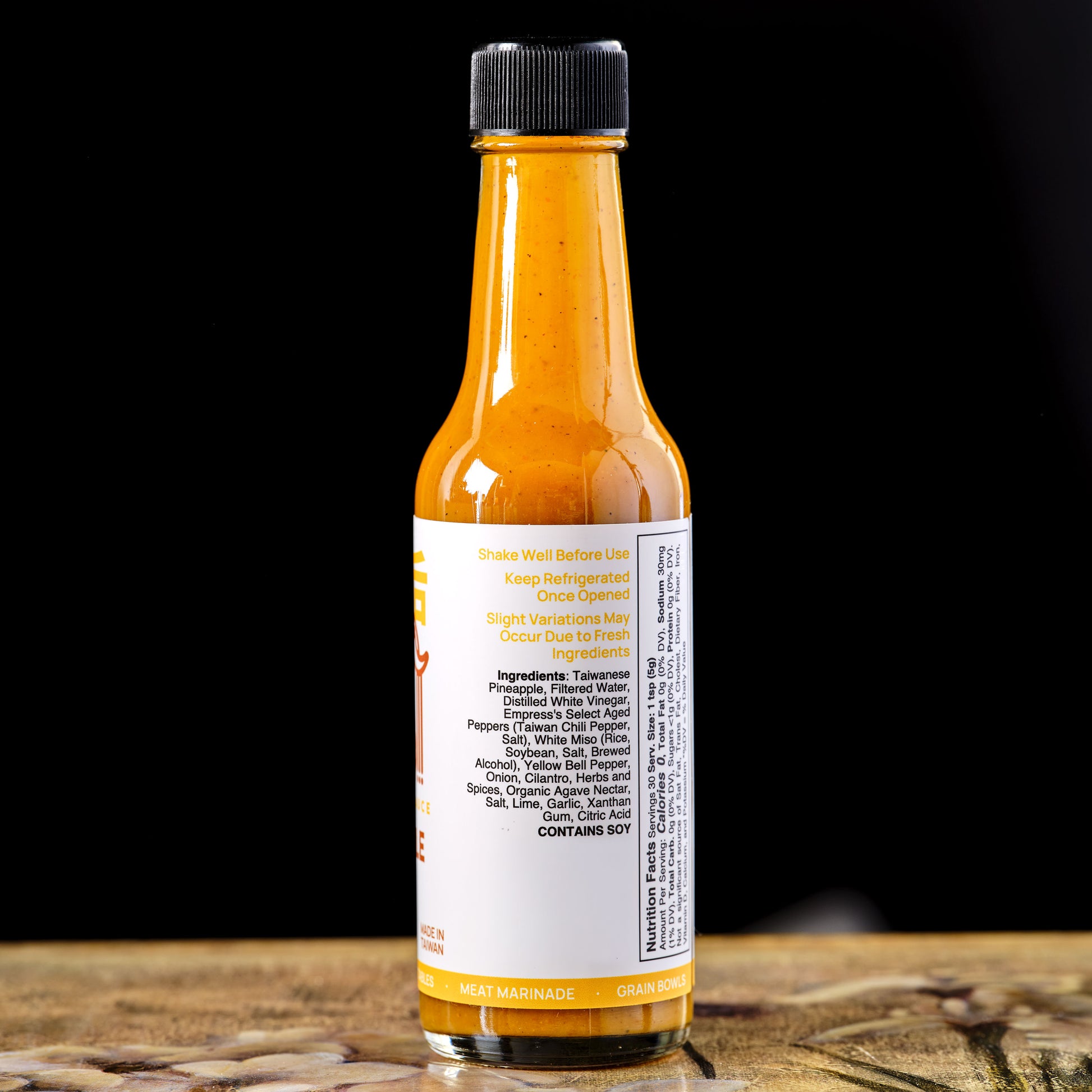 Empress Pineapple Miso Hot sauce ingredients bottle with label on a wooden surface and black background
