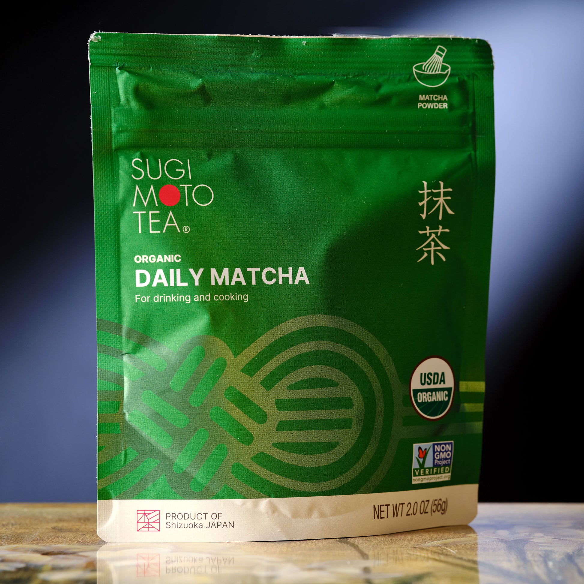 Green package of Sugi Moto Tea Organic Daily Matcha on a reflective surface with a gradient background.