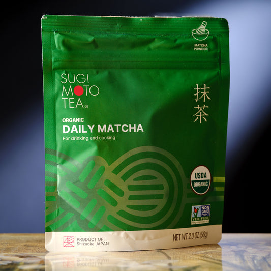 Green package of Sugi Moto Tea Organic Daily Matcha on a reflective surface with a gradient background.