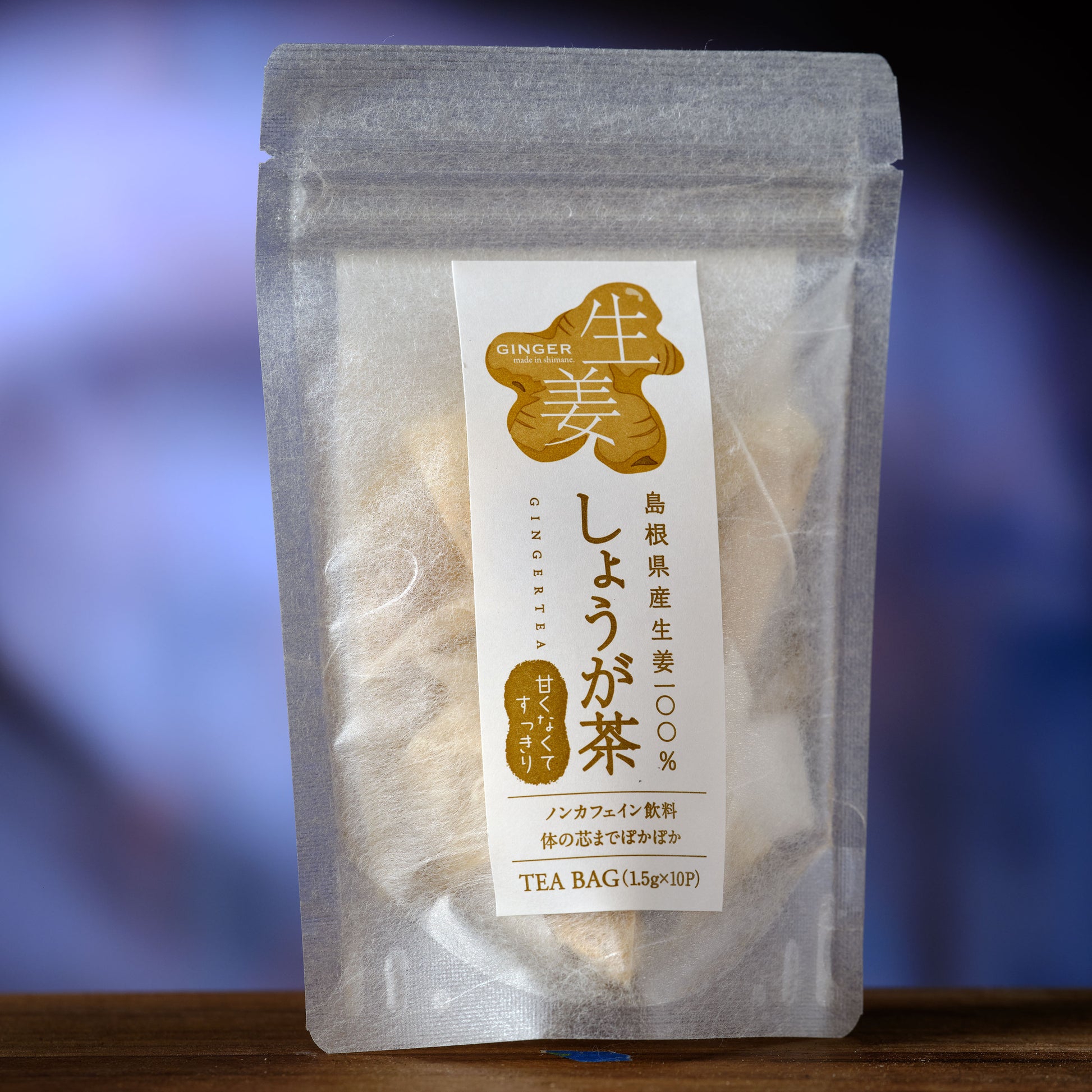 Japanese Ginger Tea  Tea bag package with a clear front, showing tea leaves inside, on a blurred blue background.